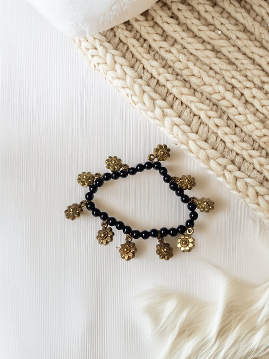 Black beaded bracelet with gold floral charms on a textured white surface