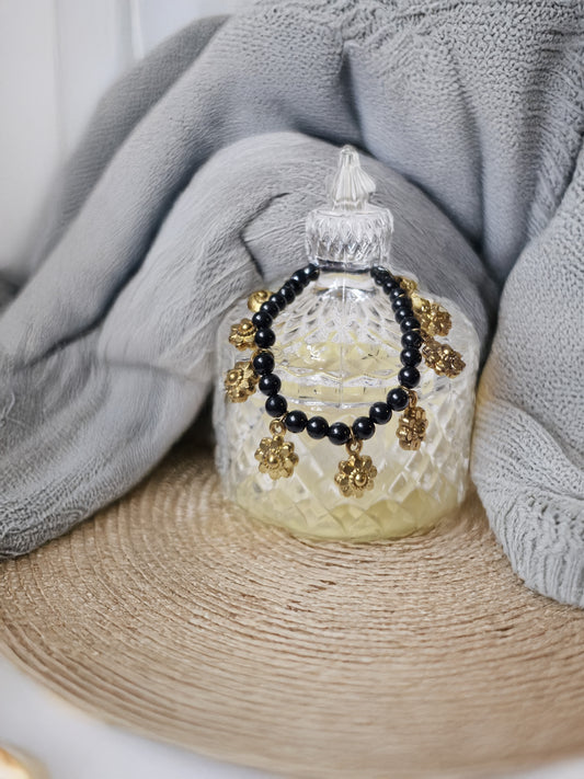 Decorative glass bottle with black and gold beads on a textured surface with gray fabric in the background