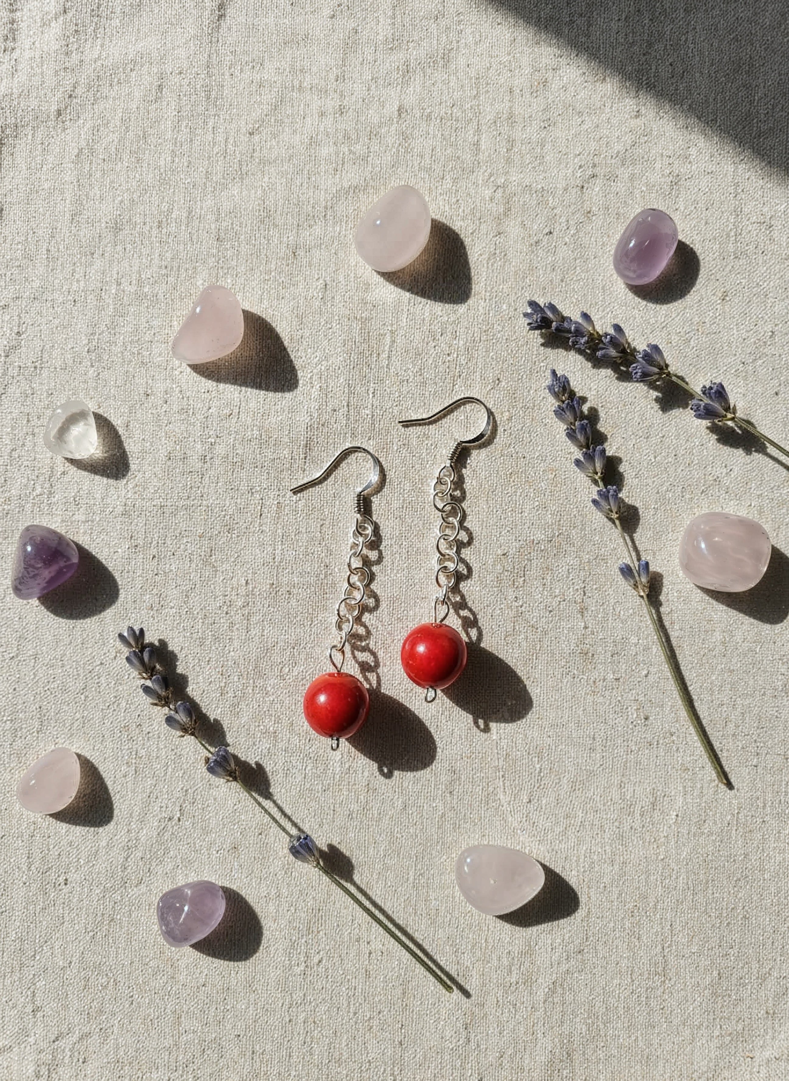 Pair of earrings with red beads on a textured surface with lavender and crystals.