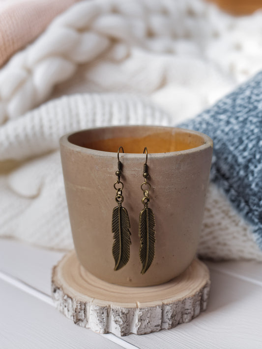 Feather-shaped earrings on a wooden stand with a ceramic cup in the background