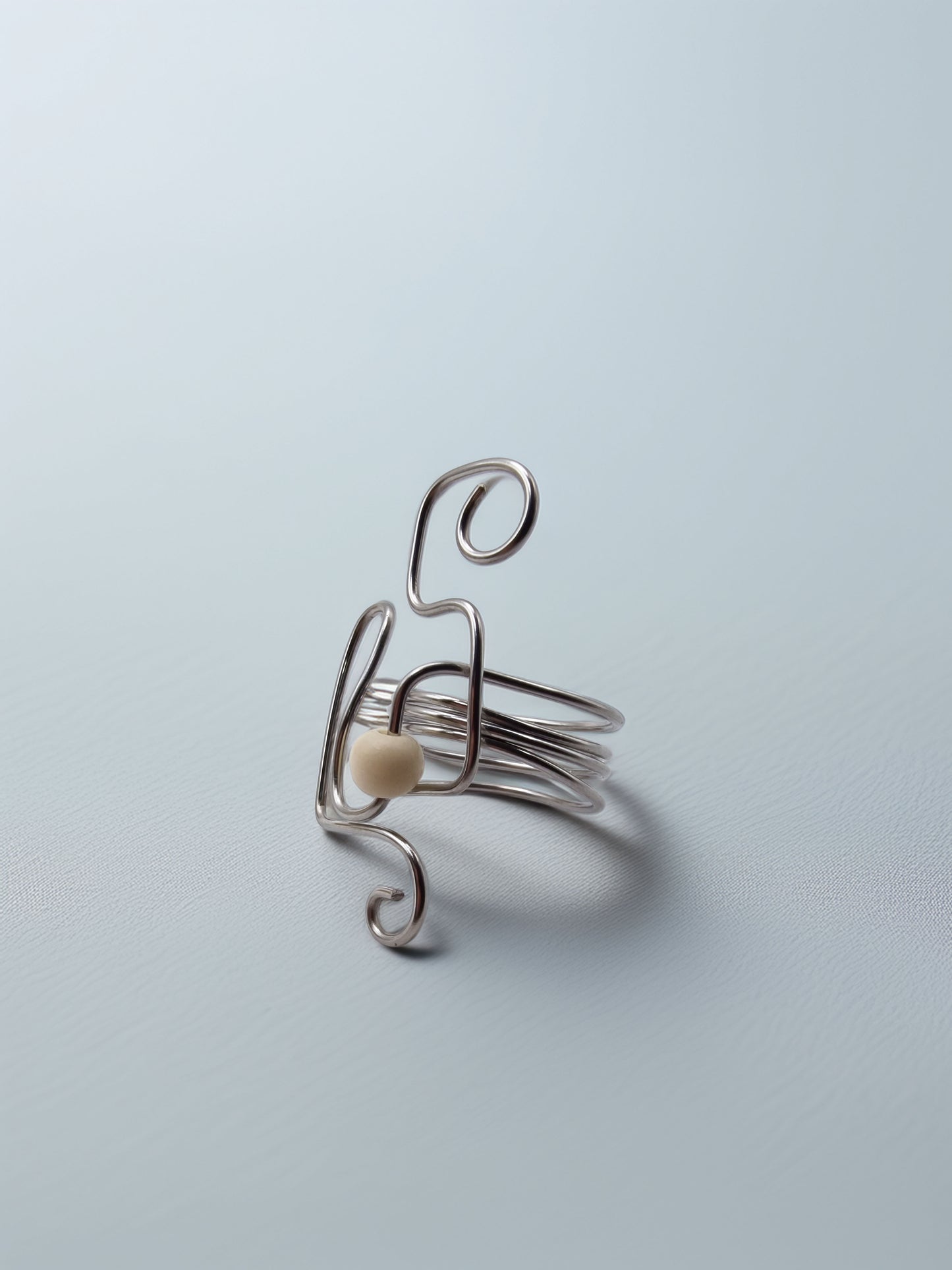 Silver wire ring with an ivory glass bead on a light blue background