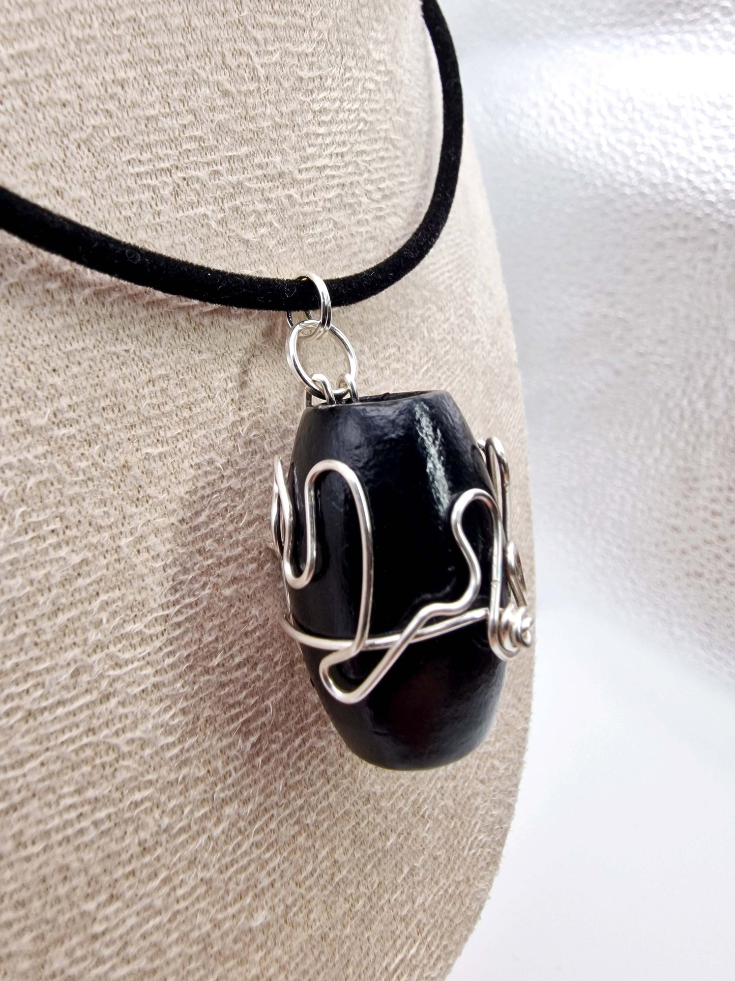 Black stone pendant with silver wire wrapping on a black cord against a neutral background