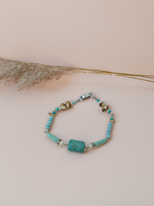 Turquoise beaded bracelet on a beige background with dried grasses.