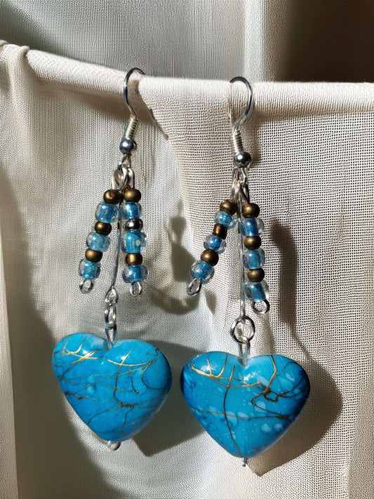 Blue heart-shaped earrings with beaded accents on a beige fabric background