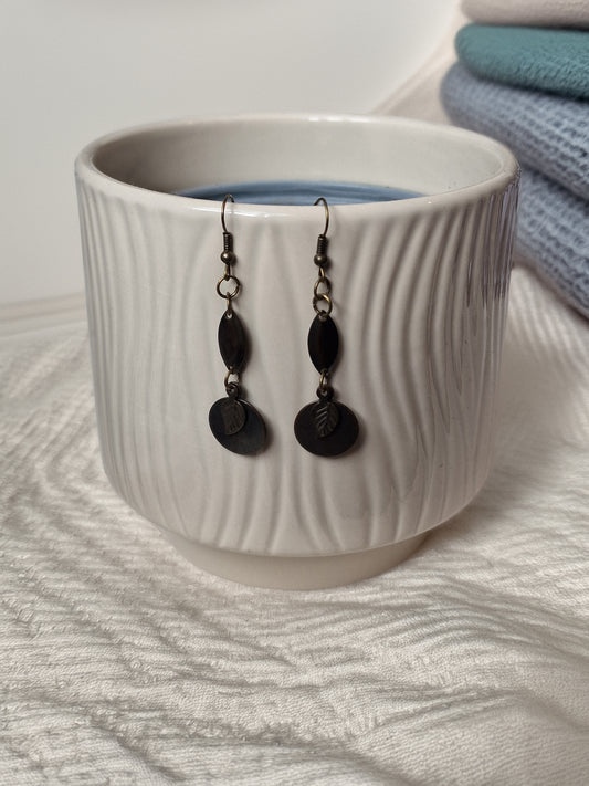 Black earrings hanging from a white textured cup on a light fabric background