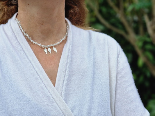 Person wearing a white robe with a pearl necklace in an outdoor setting