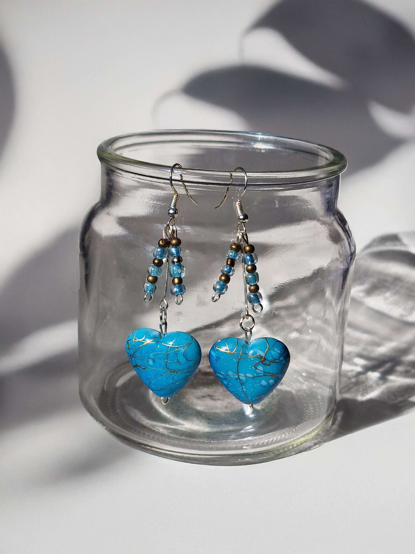 Turquoise heart-shaped earrings on a clear glass jar with a white background