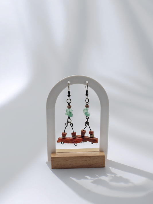 Pair of earrings on a wooden stand against a white background