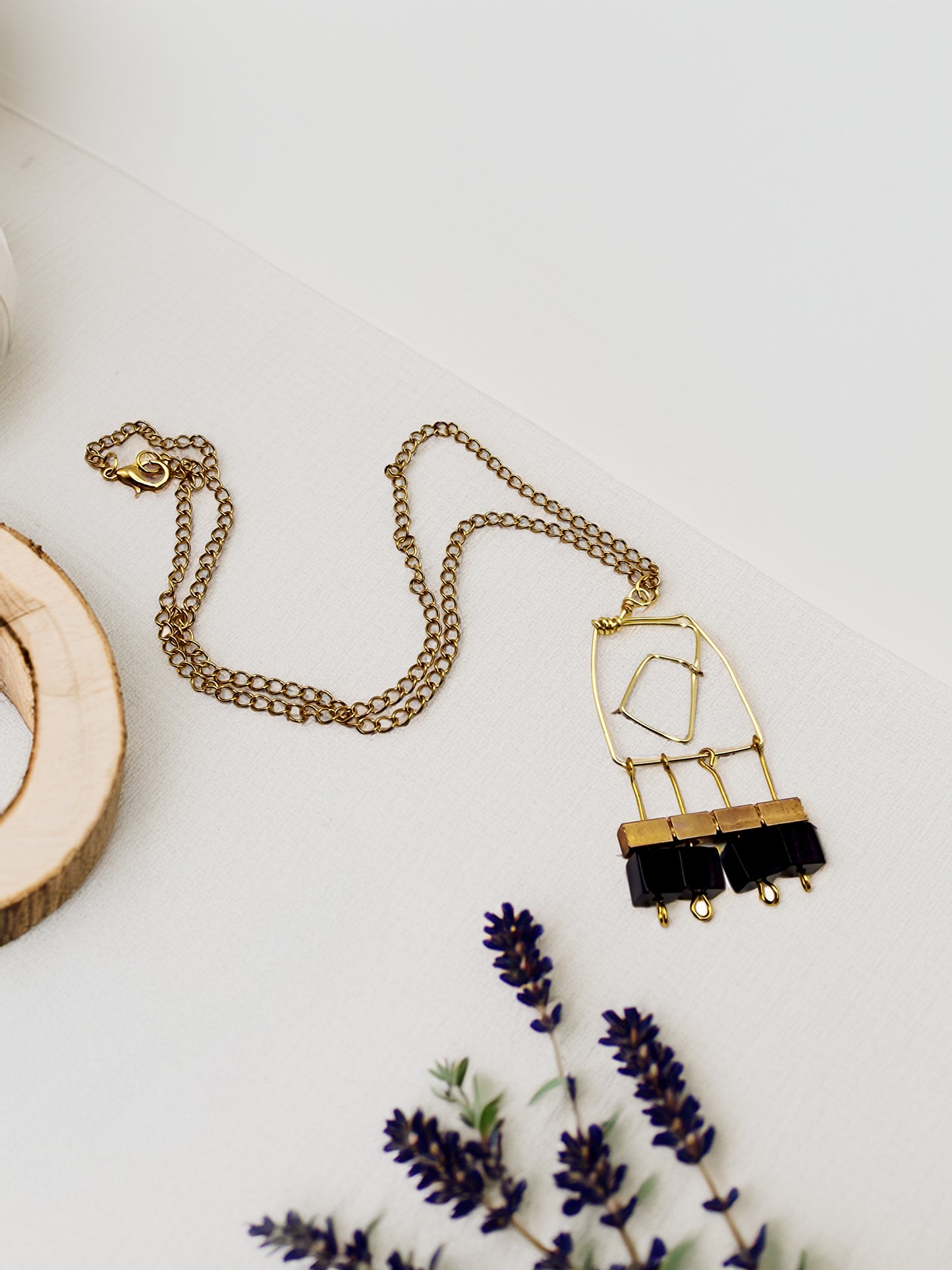 Gold necklace with black pendant on a white surface with lavender flowers