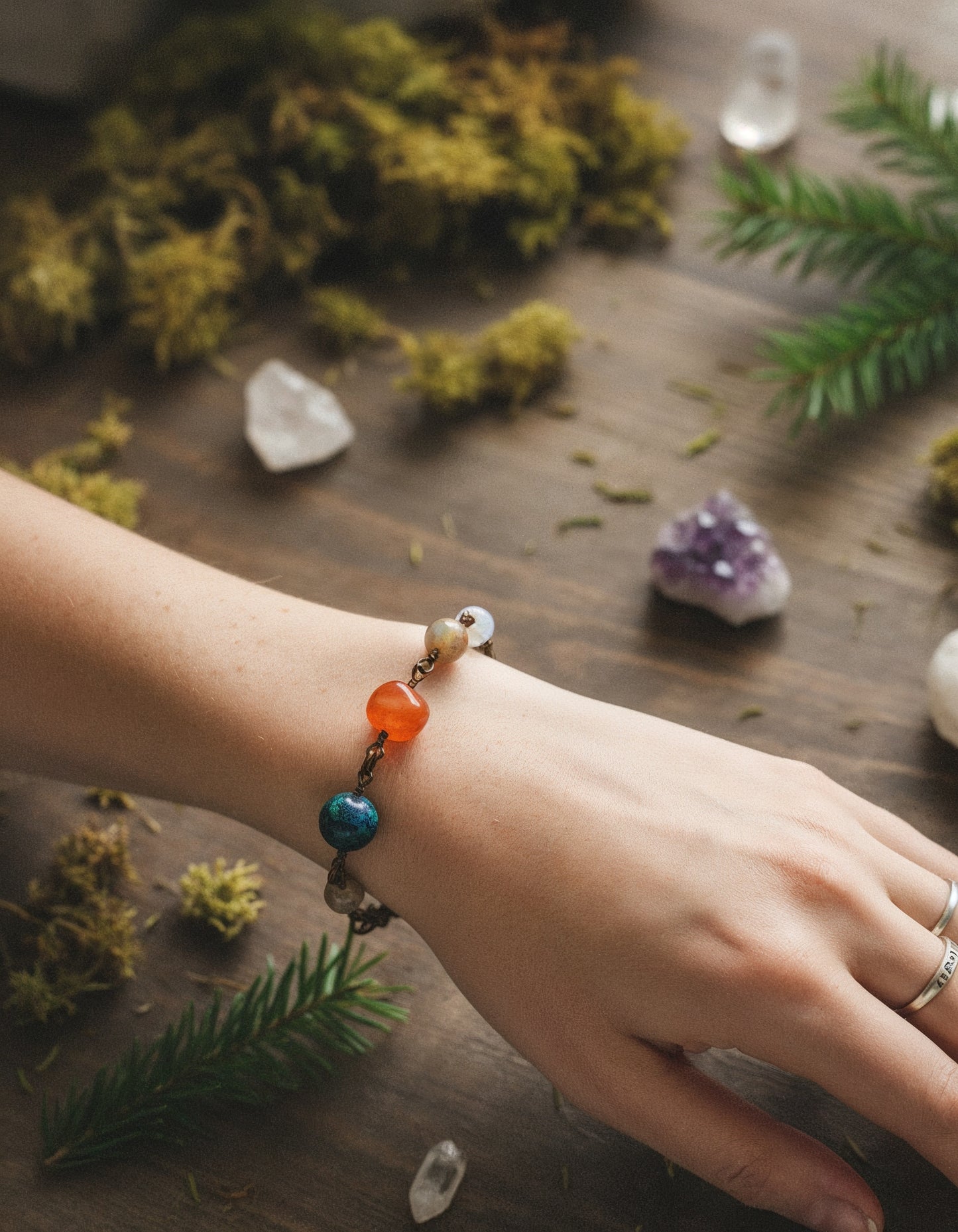 Hand wearing a colorful beaded bracelet on a wooden surface with crystals and greenery