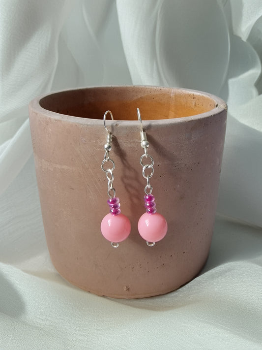 Pink beaded earrings with silver hooks in a pink pot on a white fabric background