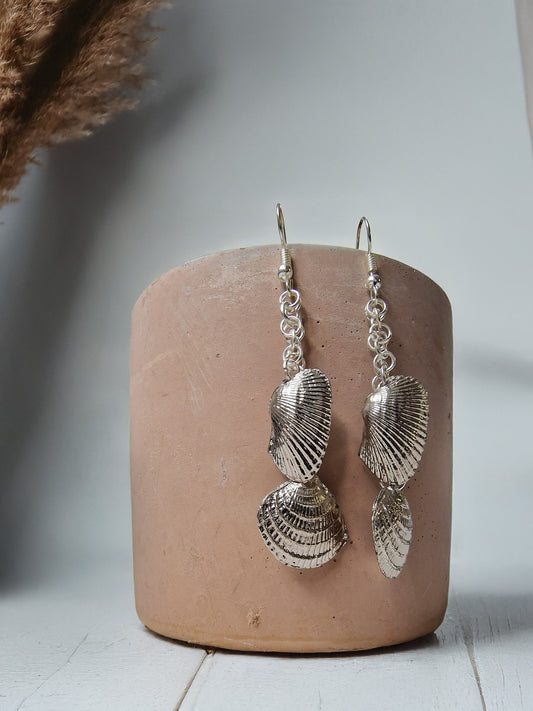 Silver shell-shaped earrings on a pink cylindrical stand with a neutral background
