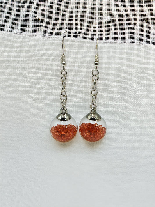 Silver earrings with orange spherical beads on a white background