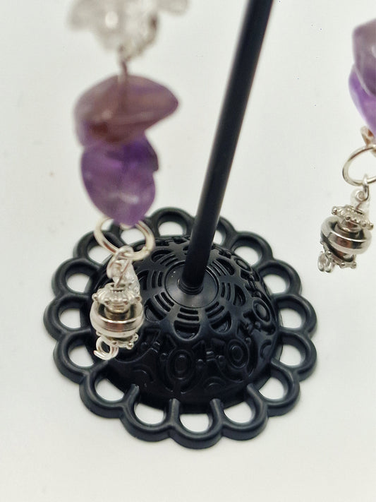 Black decorative stand with purple beads and silver charms on a white background