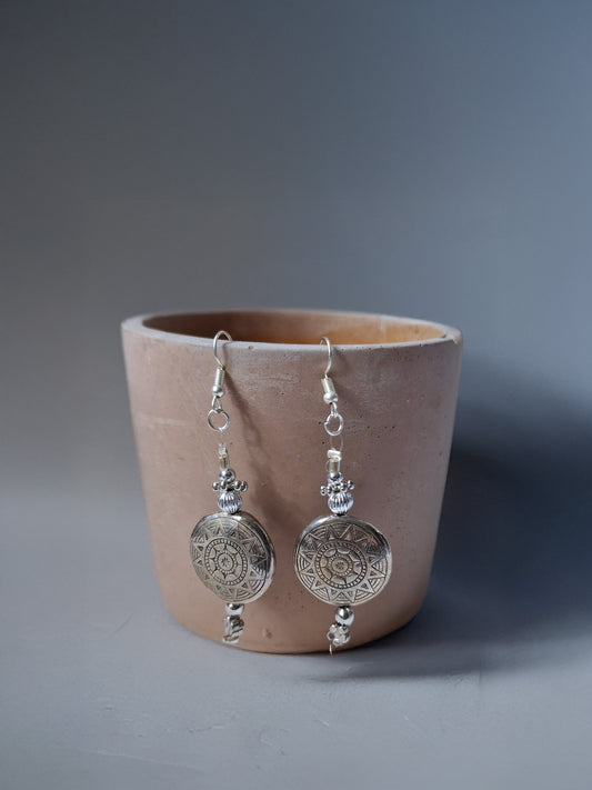 Silver earrings hanging from a pink pot on a gray background