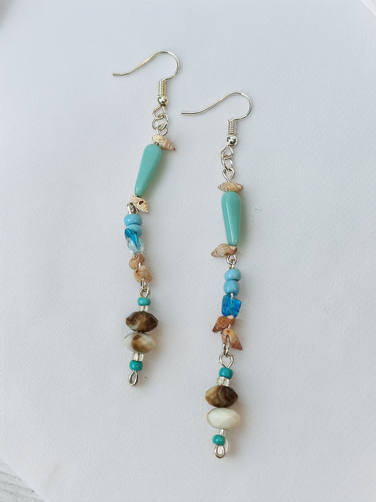 Pair of beaded earrings with turquoise, brown, and white beads on a light gray background