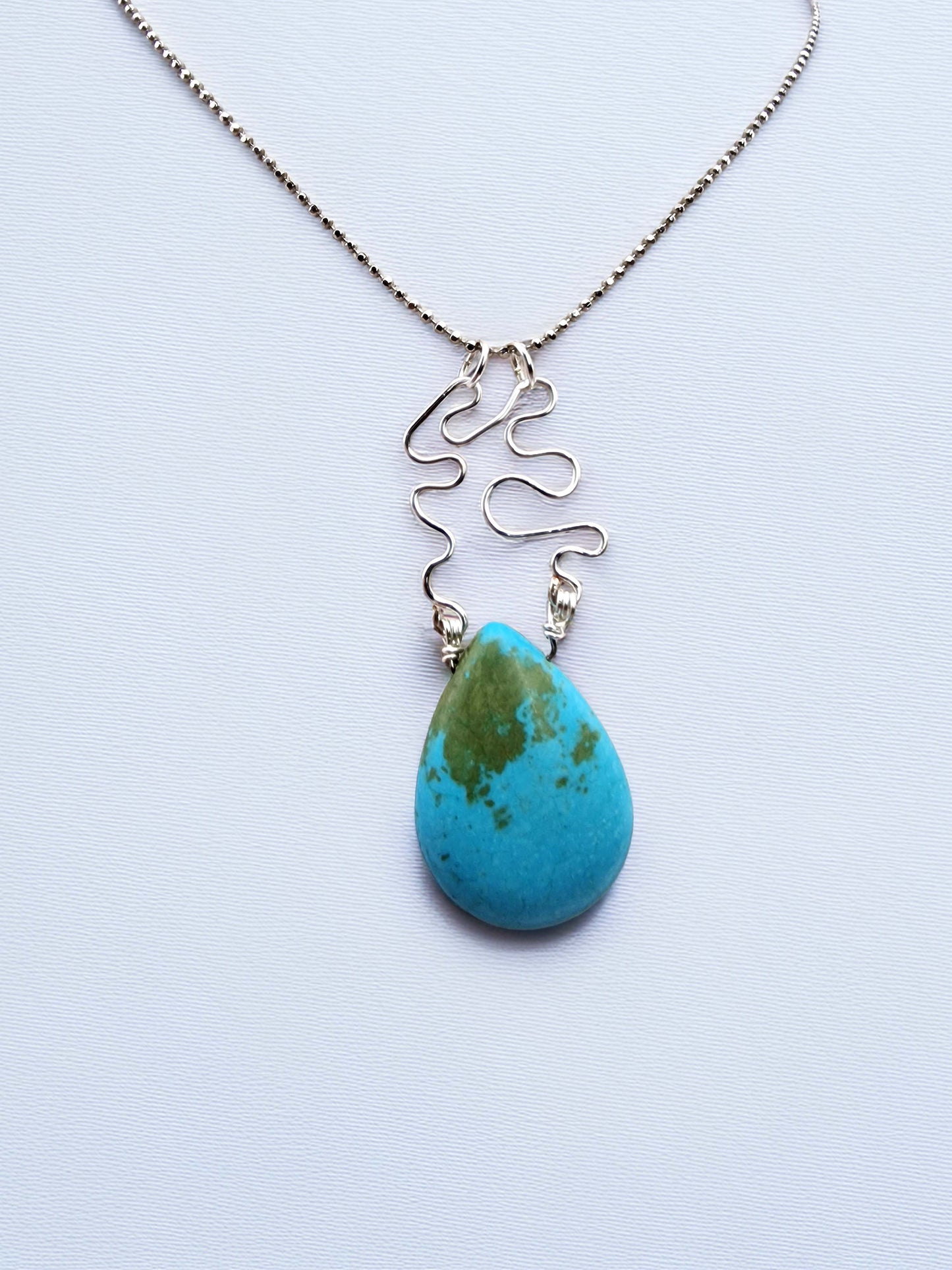Turquoise teardrop pendant necklace on a light blue background