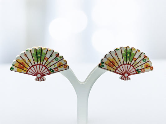 Pair of colorful fan-shaped earrings on a white stand with a blurred background