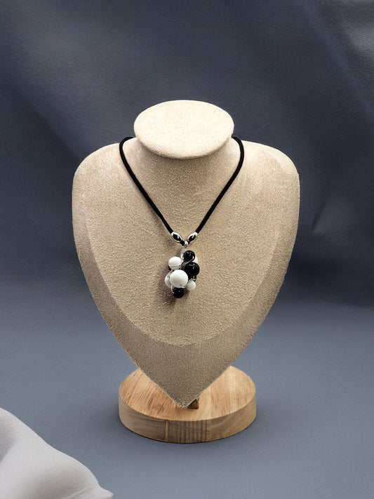 Necklace with black and white beads on a beige jewelry display bust against a dark background