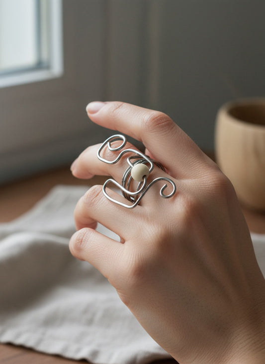 Hand wearing a unique silver ring with a wooden object in the background