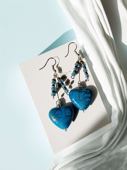 Blue heart-shaped earrings with beaded details on a light blue background