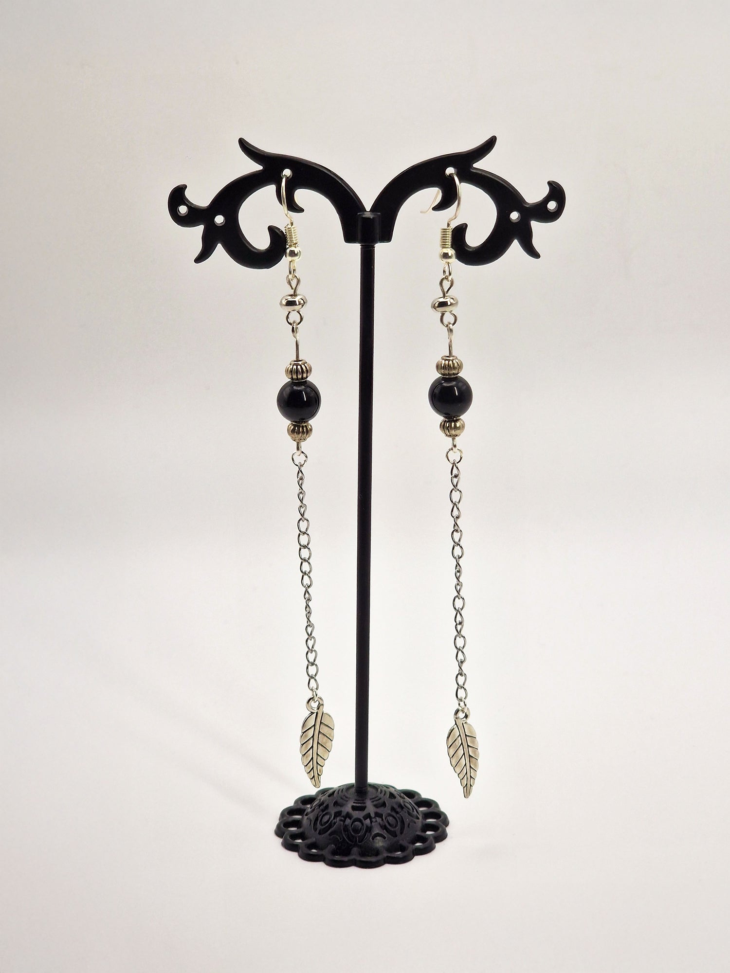 Pair of black and silver earrings on a black stand against a white background
