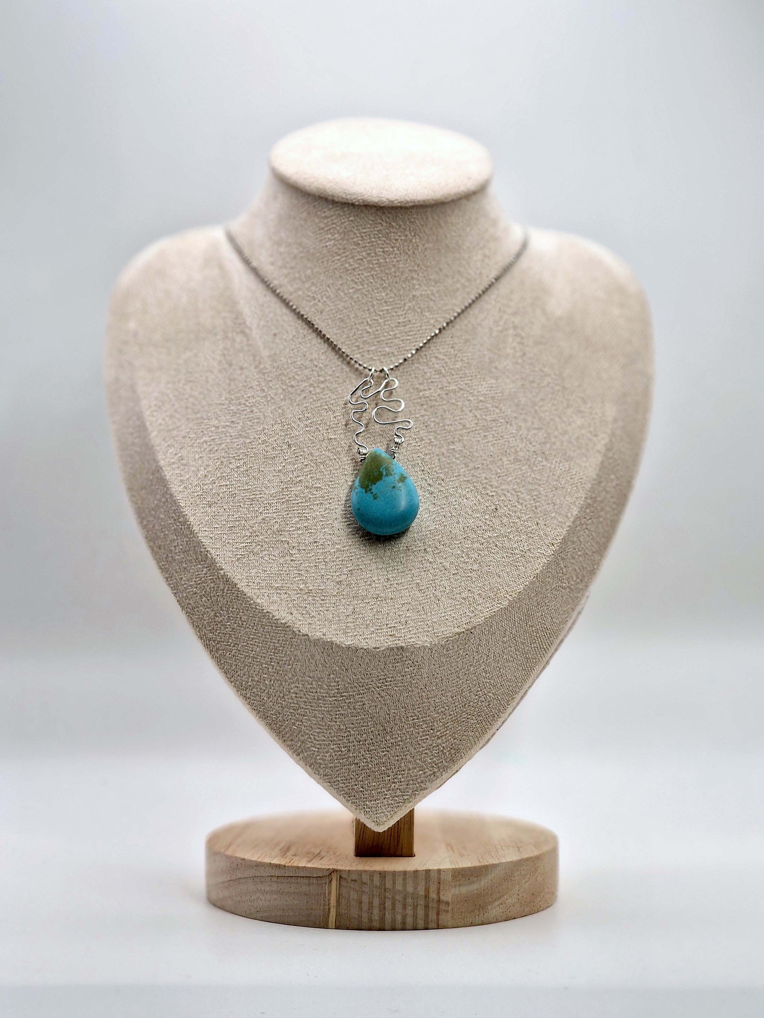 Necklace with a blue pendant on a beige bust against a white background